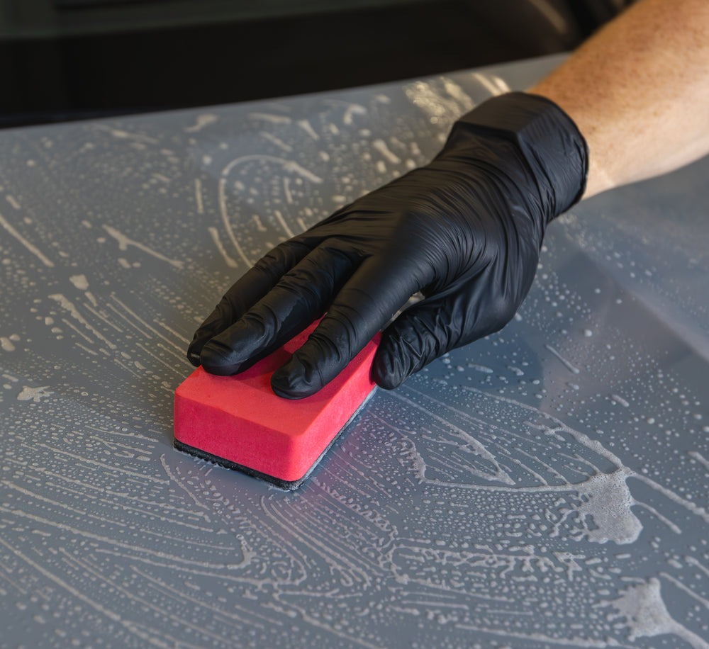 Roter Clay Sponge mit Polymerseite bei der manuellen Reinigung einer nassen Lackfläche